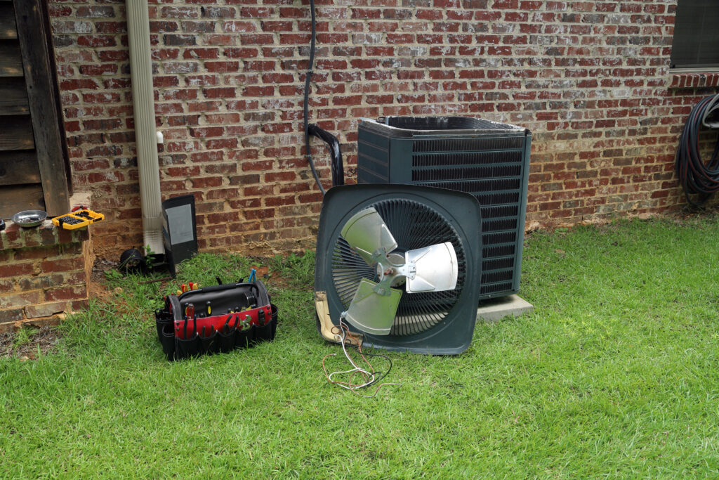 A picture of an outside air conditioning unit with the lid opened and a bag of maintenance tools laying next to it